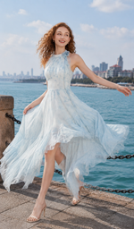 Woman twirling in a blue halter chiffon dress with an asymmetrical handkerchief hem at a sunny waterfront promenade.