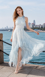 Woman wearing a blue halter handkerchief hem chiffon dress by the seaside with a flowing layered skirt and elegant silhouette.