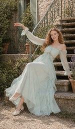 Seated model wearing the Celestine’s Waltz off-shoulder mint green dress on vintage French villa steps