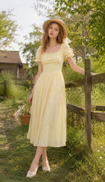 Model wearing the Daisies Before Noon Dress, holding a bouquet of daisies in a charming cottage garden.