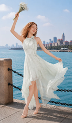 Woman smiling in a green halter chiffon dress with a flowing asymmetrical skirt beside the sea.