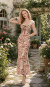 Model wearing the Letters From The Rose Garden Dress in a blooming garden, featuring a romantic floral print, corset-inspired bodice, ruffled sleeves, and elegant midi silhouette.