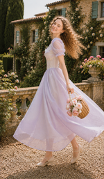 Side view of the Letters From Villa Fiora Corset Dress featuring the fitted lace corset bodice, puff sleeves, flowing lavender skirt, and floral basket.