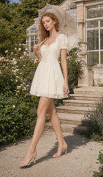 Model twirling in the Morning in Annecy Corset Dress (Short) with a lace parasol outside a greenhouse
