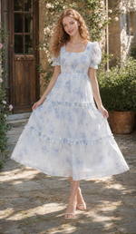 Model wearing The Blue Rose of Avignon Dress with a square neckline and blue floral ruffle skirt in a Provence garden.