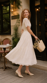 Back view of The Cream Memory Dress featuring a feminine V-back neckline, adjustable waist tie, delicate floral embroidery, and flowing midi skirt in a romantic café setting.