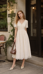 Woman wearing The Cream Memory Dress in ivory outside a charming European-style café, featuring a romantic V-neck silhouette and delicate embroidery.