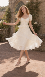 Model wearing The Last Promise of Ravello ivory textured midi dress beside a stone garden balustrade