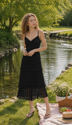 Model standing in a garden wearing The Last Summer Diary Dress in black, featuring adjustable spaghetti straps, layered lace hem, lightweight fabric, and romantic feminine silhouette.