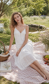Model wearing The Last Summer Diary Dress in white while relaxing on a picnic blanket by the lake, featuring lace trim, tiered skirt, and romantic summer styling.