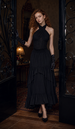 Model standing at ornate iron doors wearing The Last Vow Corset in black, highlighting the structured floral lace bodice, halter neckline, and dramatic layered skirt.