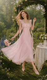 Model in The Rose Oath Dress in pink with ruffle straps and a flowing midi skirt in a dreamy garden setting.