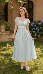 Model holding a bouquet of roses while wearing The Seventh Letter Corset Dress featuring embroidered chiffon, lace neckline, puff sleeves, ribbon waist, and flowing romantic silhouette.