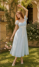 Portrait of a model wearing The Seventh Letter Corset Dress featuring a soft blue embroidered fabric, delicate lace neckline, puff sleeves, feminine ribbon waist tie, and vintage-inspired elegance.